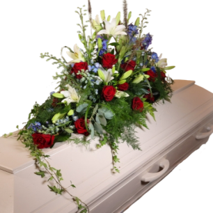 Vit kista med ett blomsterarrangemang av röda rosor, vita liljor och blå blommor ovanpå.