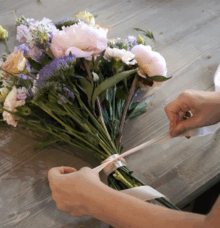 Händer knyter ett band runt en bukett med blommor på ett bord.