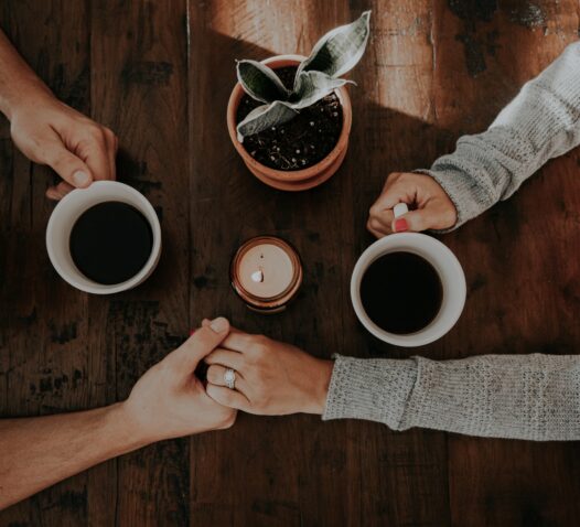 Tre personer vid ett bord, två dricker kaffe och en håller hand.
