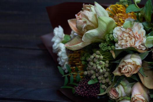 En bukett med olika blommor inklusive rosor och gröna blad på ett mörkt bord.