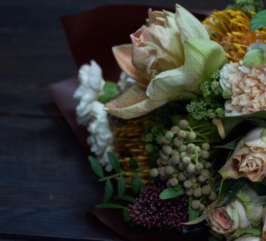 En bukett med olika blommor inklusive rosor och gröna blad på ett mörkt bord.